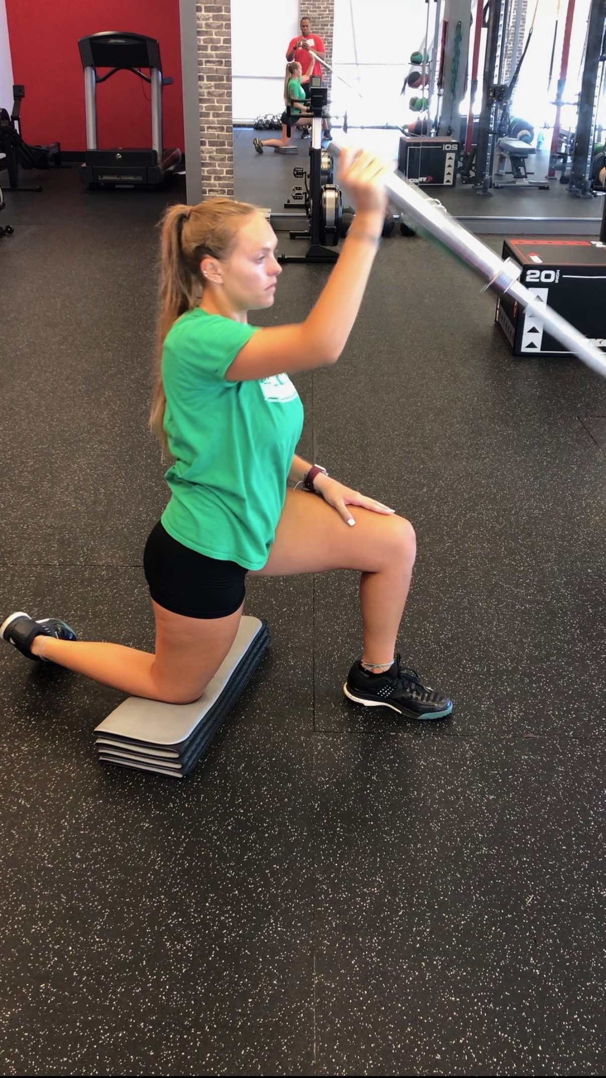 Client performing a kneeling lunge exercise with a barbell in the gym